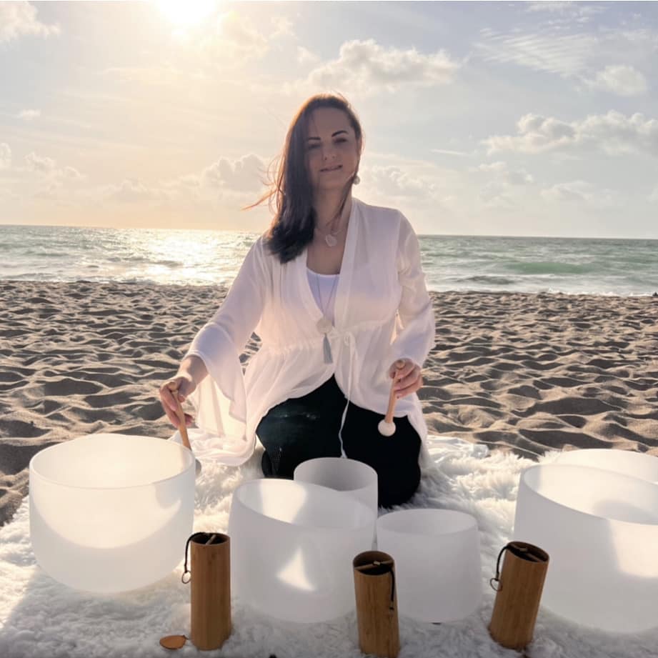Julie King seating on the beach with sound bowls and koshi chimes